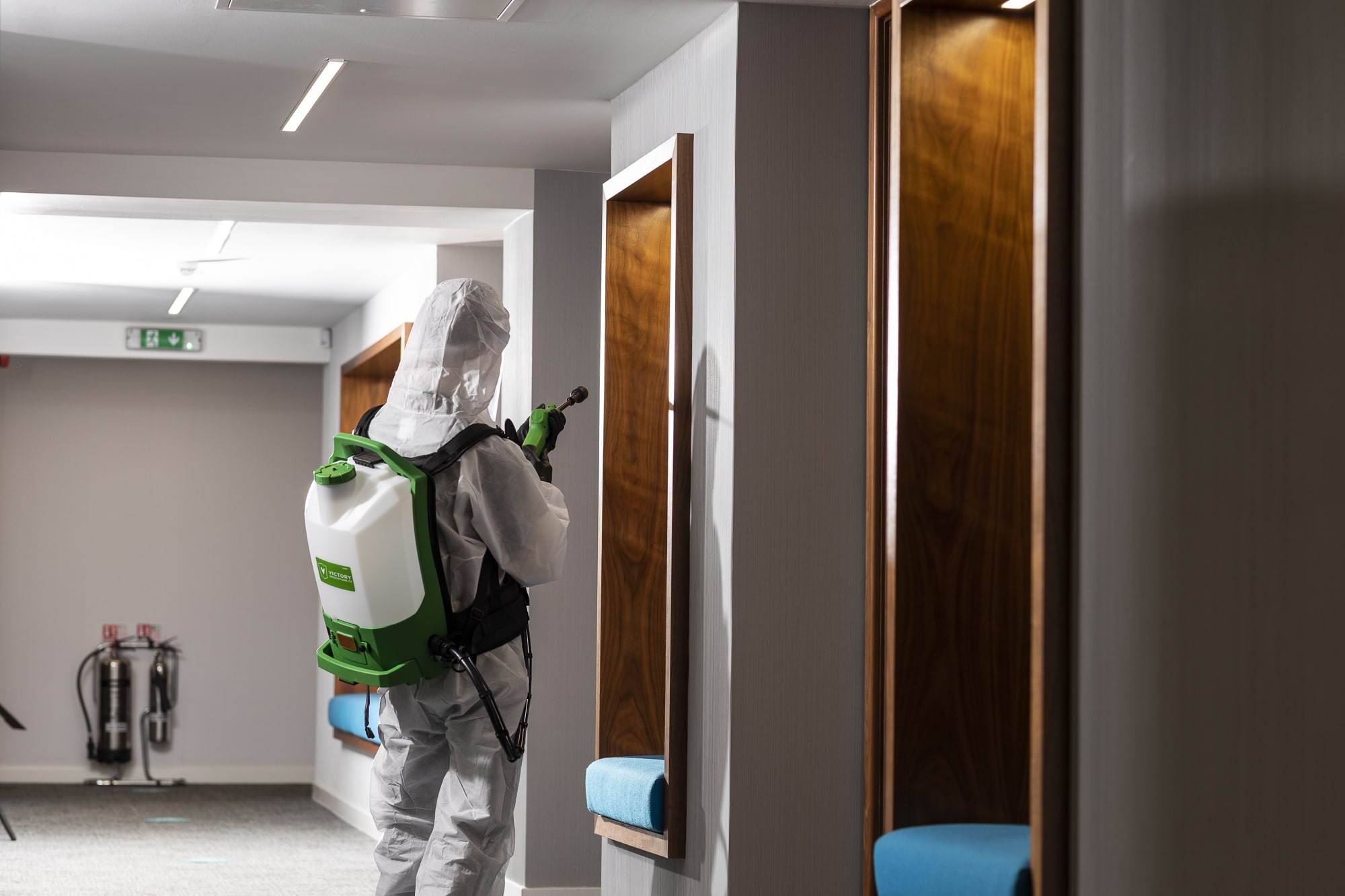 Man in protective suit spraying disinfectant in office corridor against Covid-19