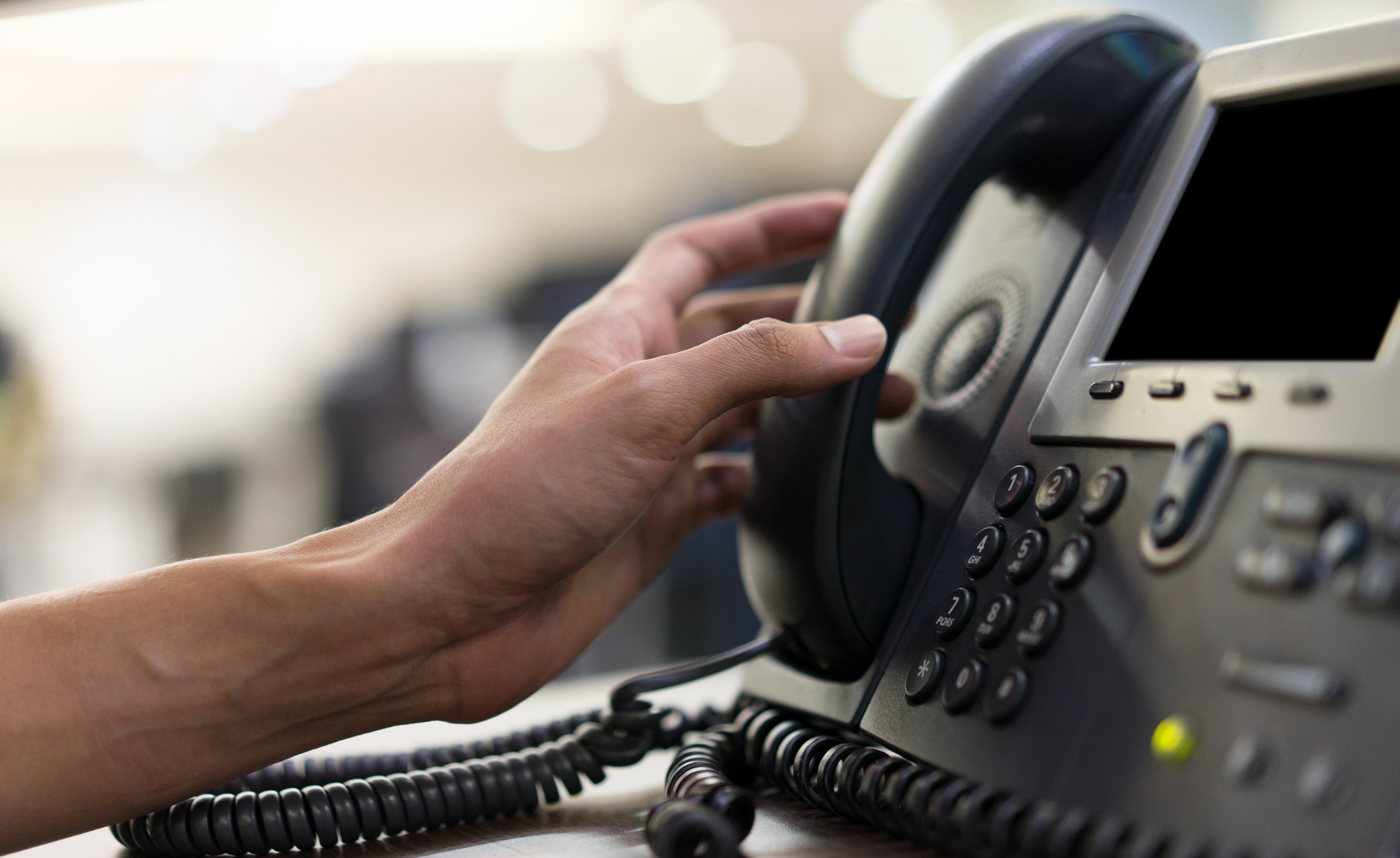 close up employee man hand touching handset of  telephone on desk for contact customer or receiving call , hotline  concept